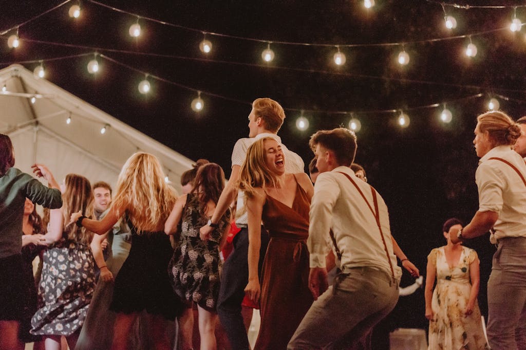A lively outdoor night party with people dancing under string lights.
